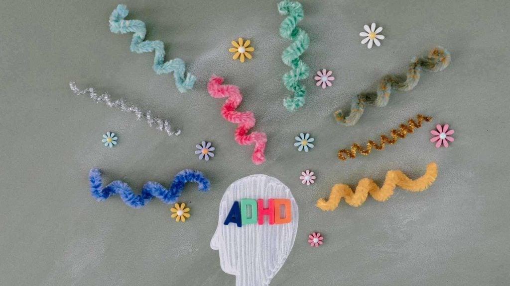 A visual depiction of an ADHD mind using a chalk-drawn head with flowers and twisted pipe cleaners representing thoughts