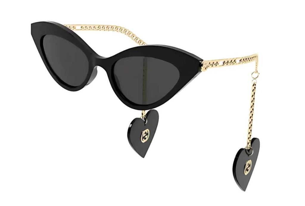 Gucci GG0978S cat-eye sunglasses in black with dark lenses, a dainty gold chain, and dangling hearts