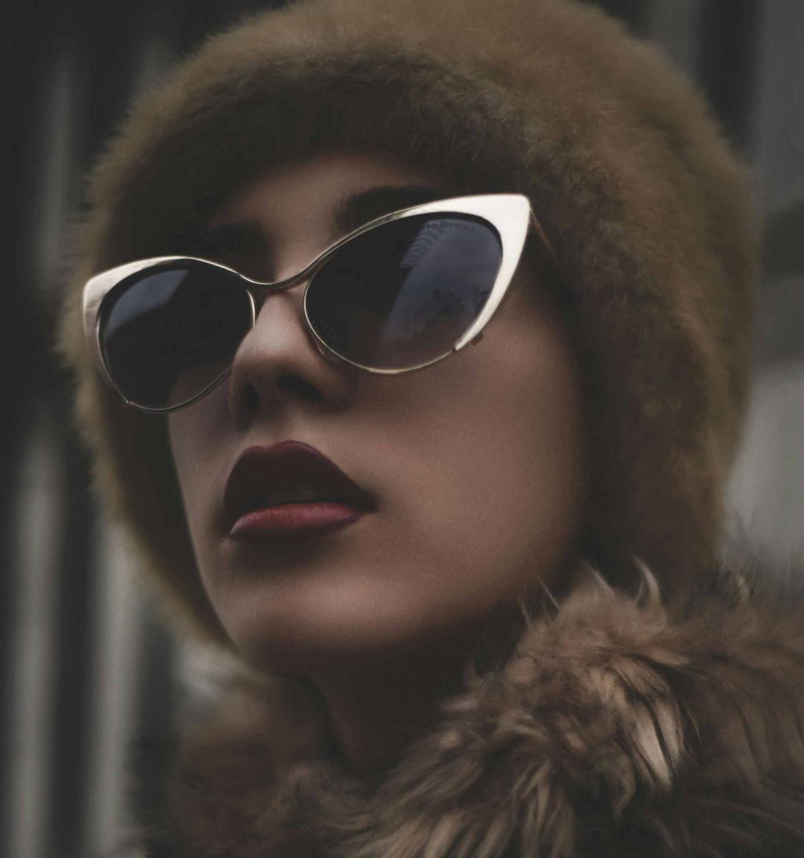 A woman wearing gold cat-eye sunglasses with a fur coat and hat