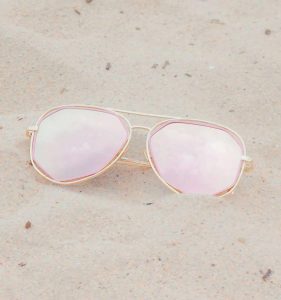 Trendy pink aviator sunglasses lying on a sandy beach