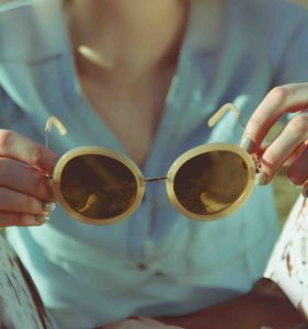 A woman holding stylish oversized round sunglasses with thick pale yellow frames