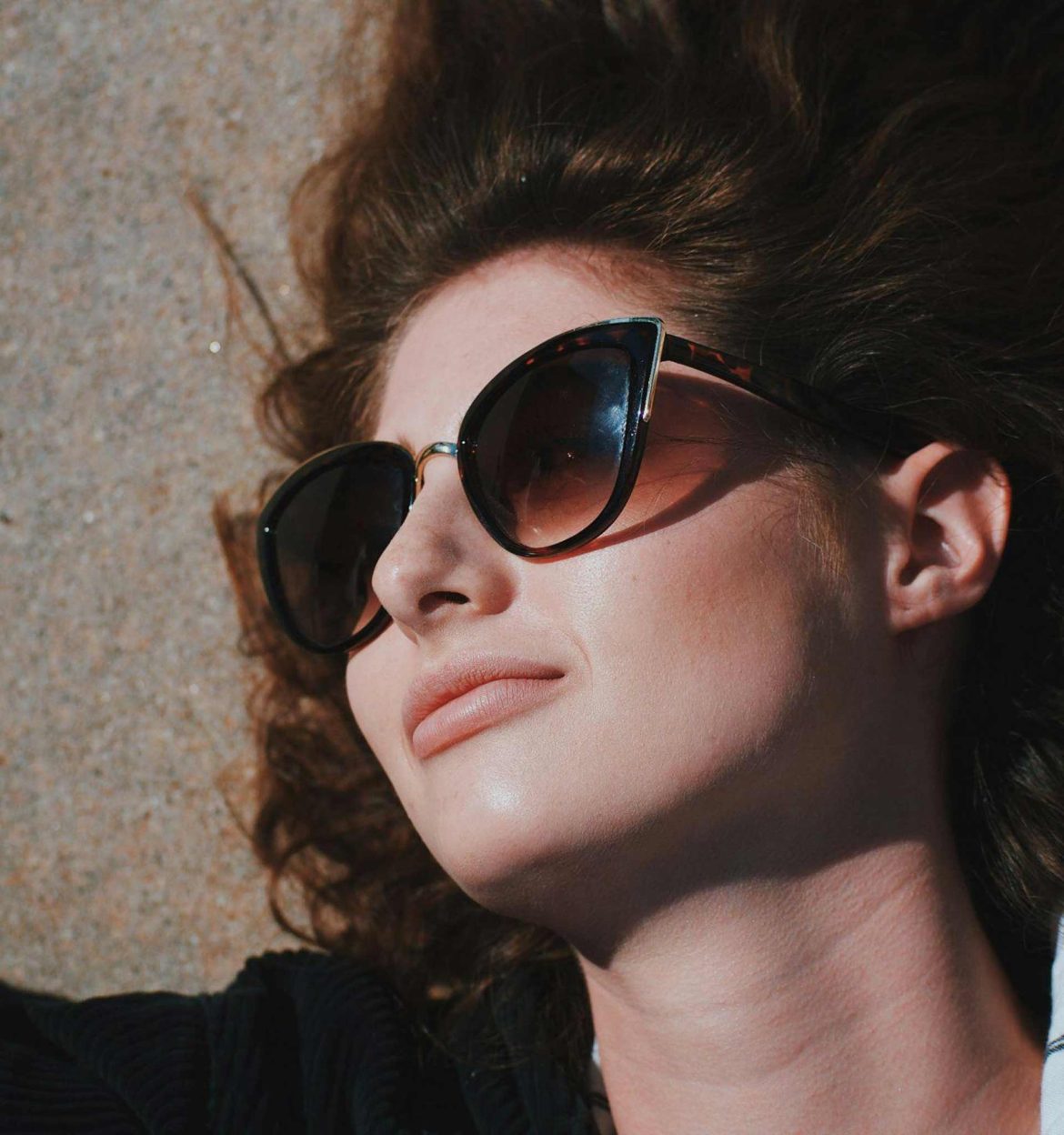 A brunette woman wearing bold cat-eye tortoise shell sunglasses with gold accents